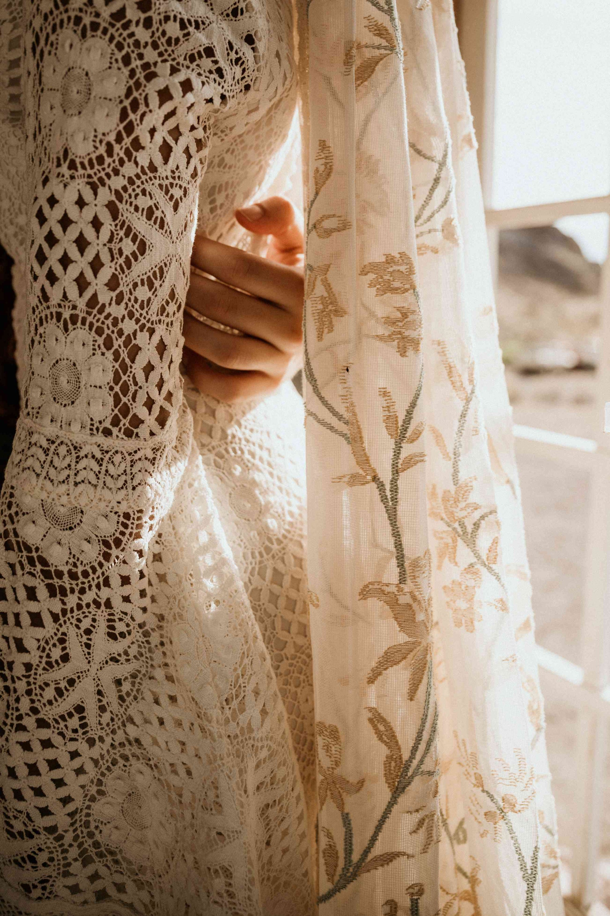 A groom holding the back of a bride wearing a modern lace wedding dress and colourful veil.