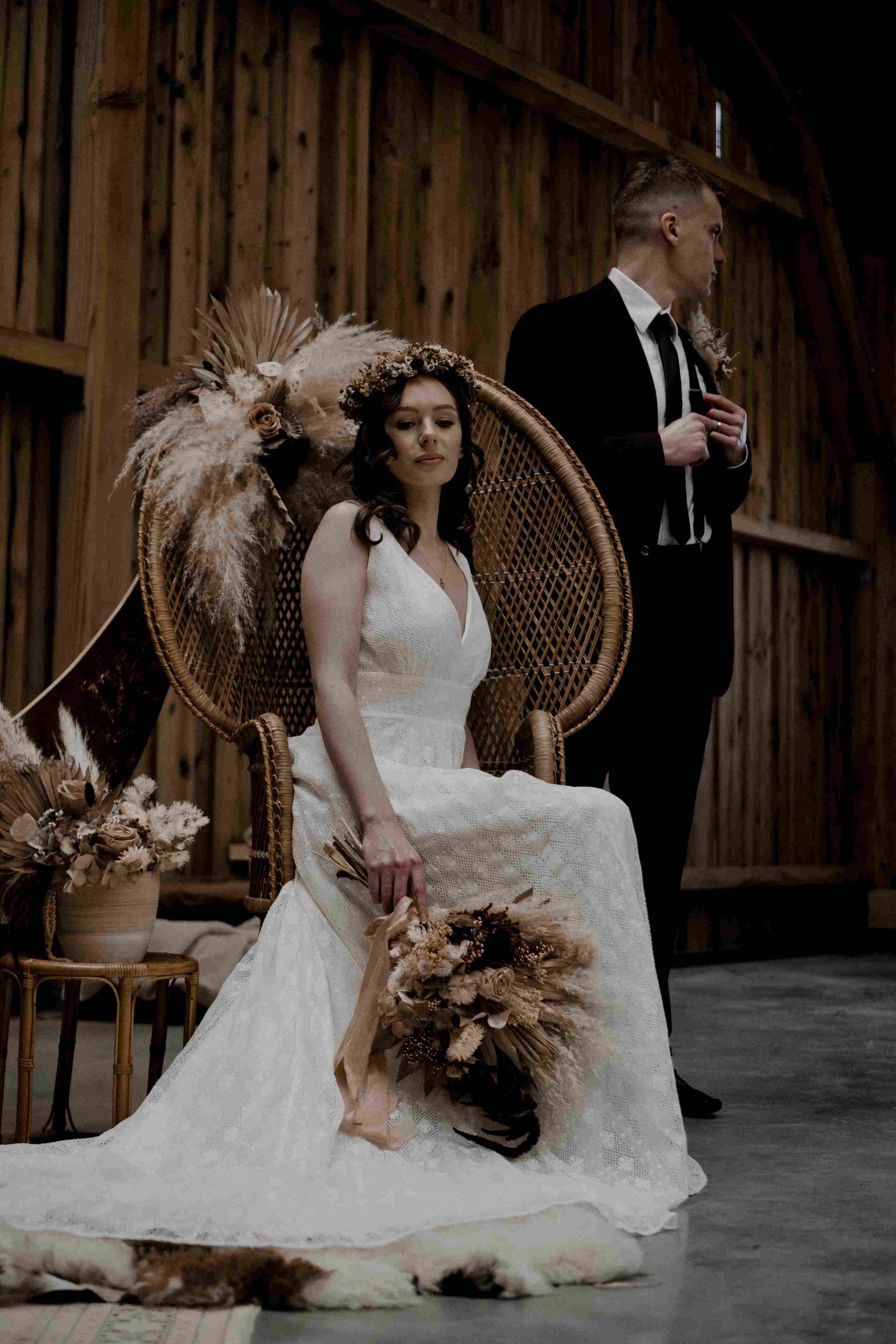 bride wearing a lace dress and sitting on a peacock chair with the groom standing in the background