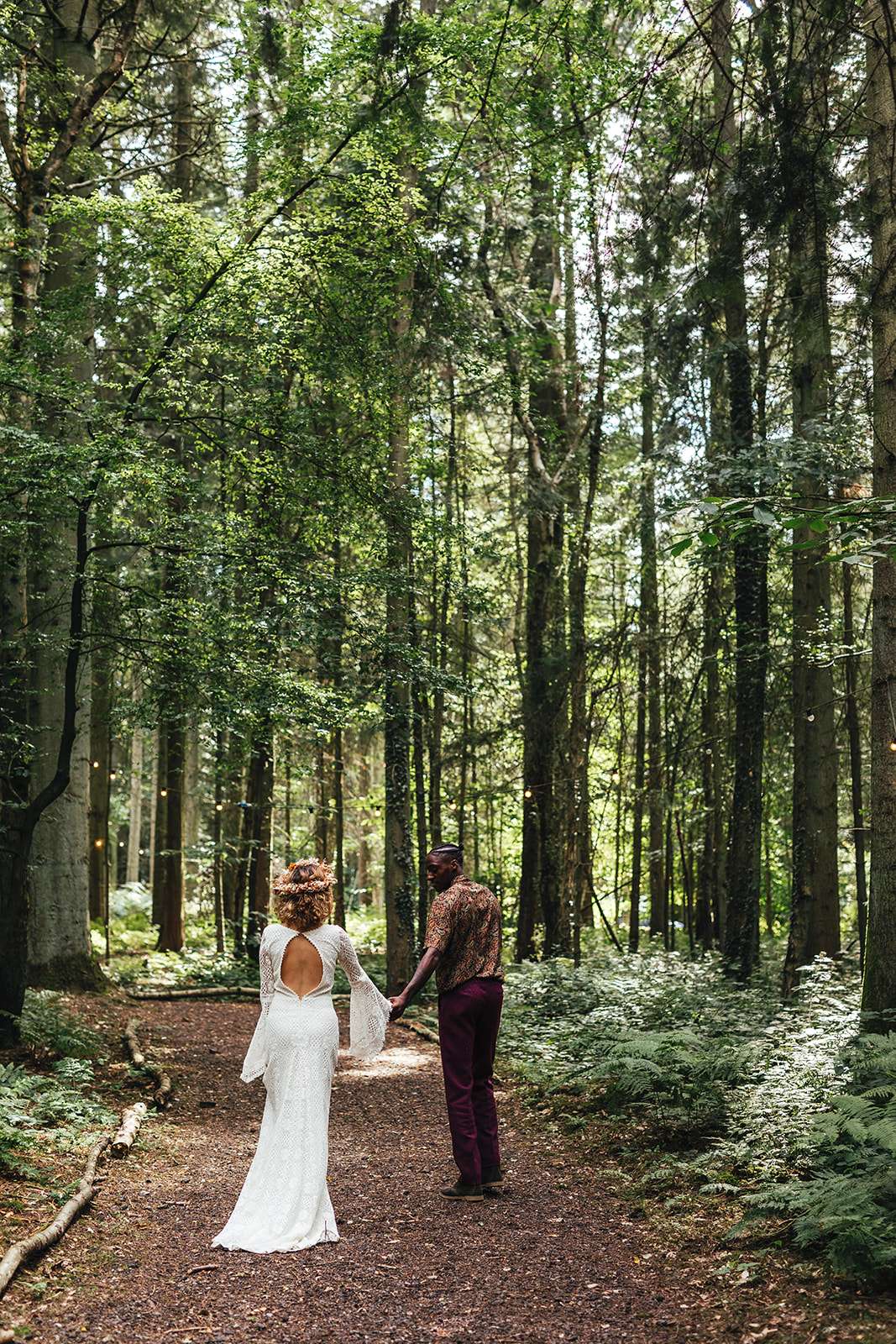 bohemian bride and groom walking hand in hand in a forest woodland wedding