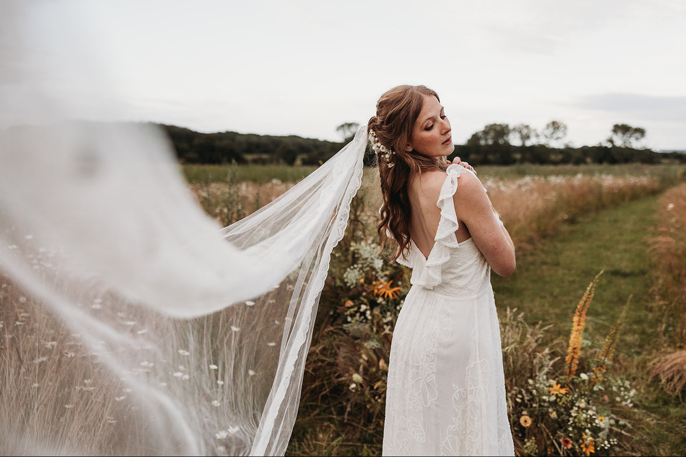 Model wearing a modern bohemian wedding dress and a veil on a field.
