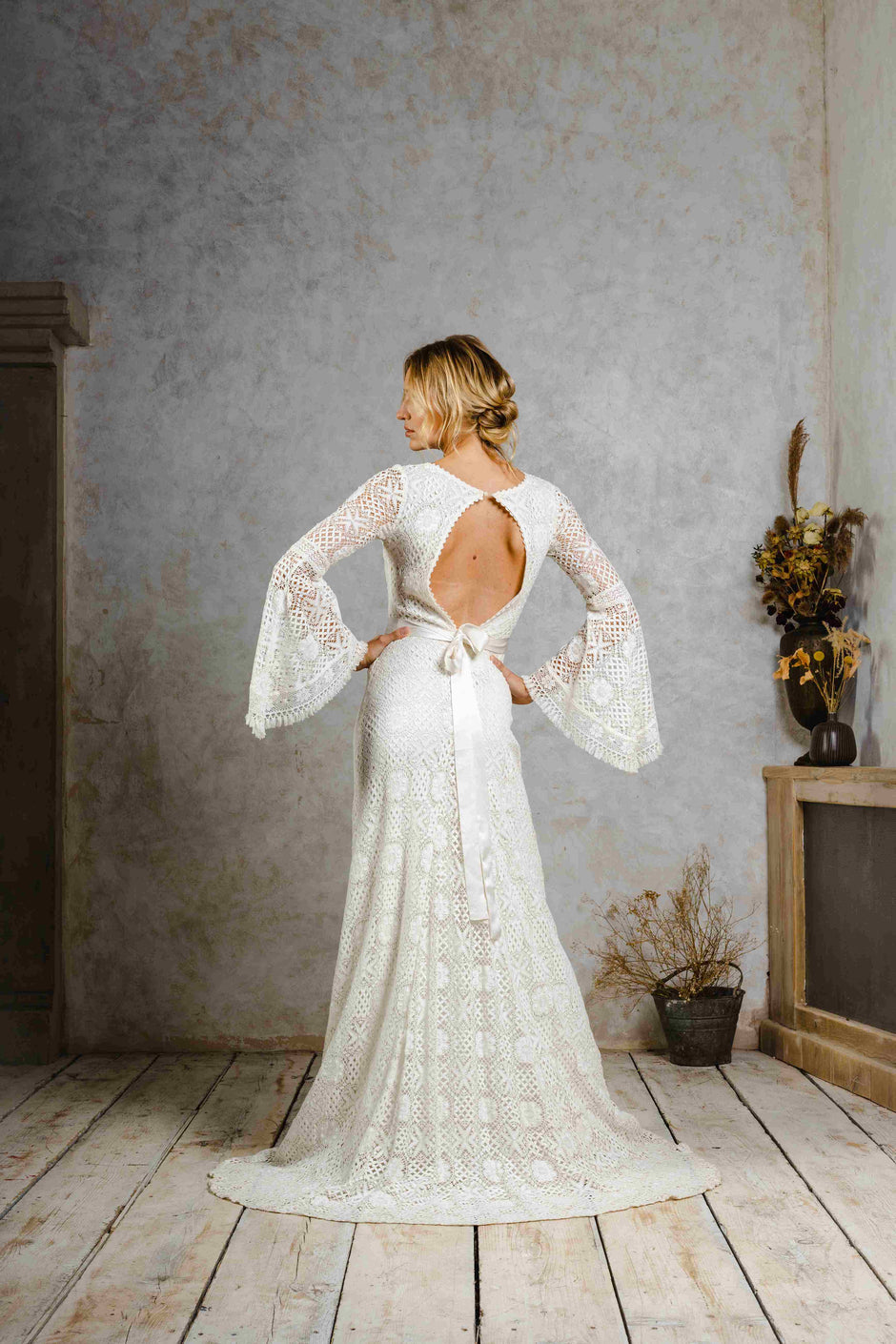 Model wearing a modern bohemian lace wedding dress with bell sleeves.